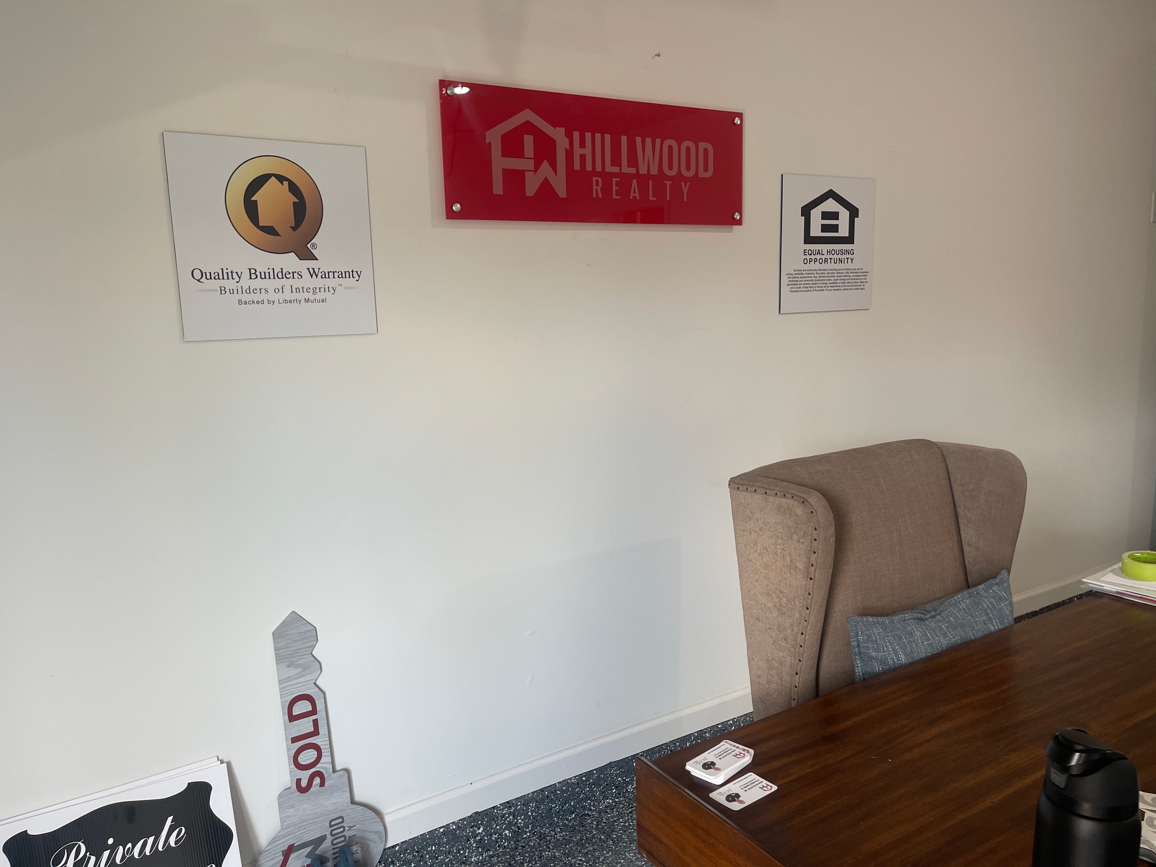 Hillwood Realty branded office wall display with acrylic sign and real estate yard signs