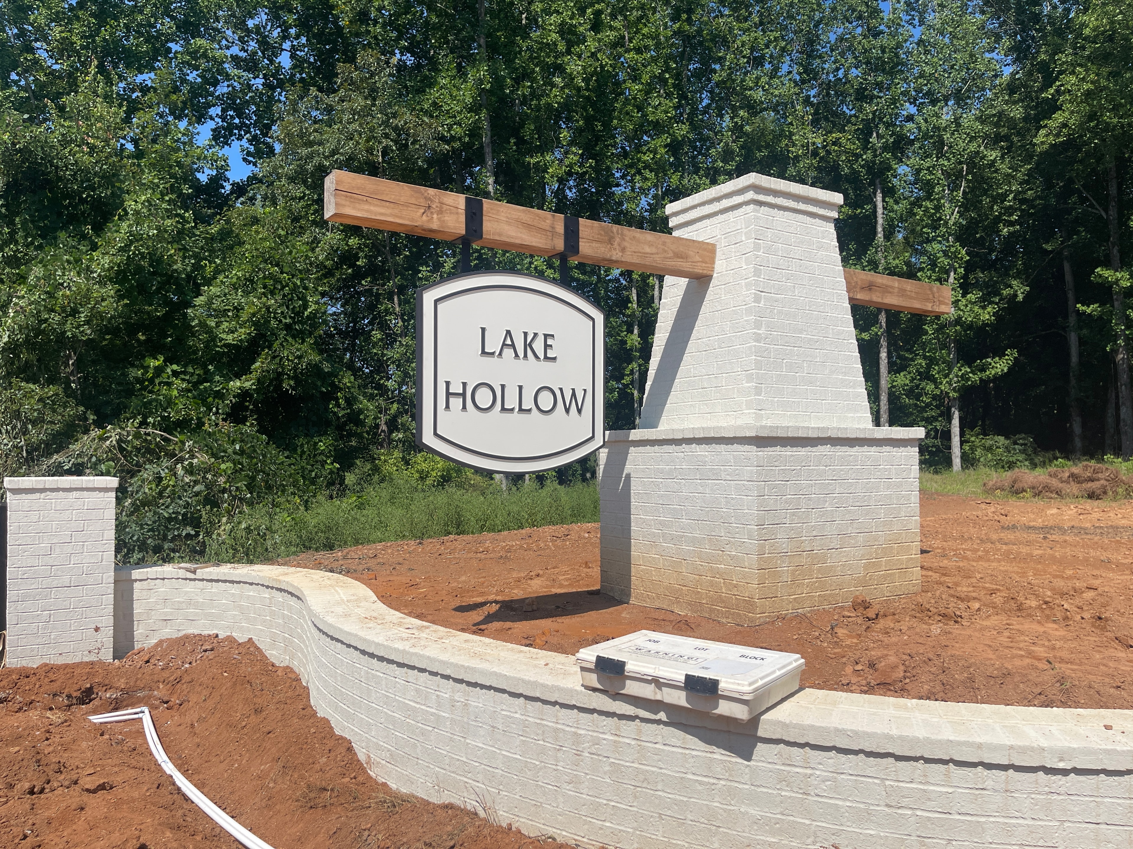 Lake Hollow community entrance monument sign hanging from timber beam between white brick pillars