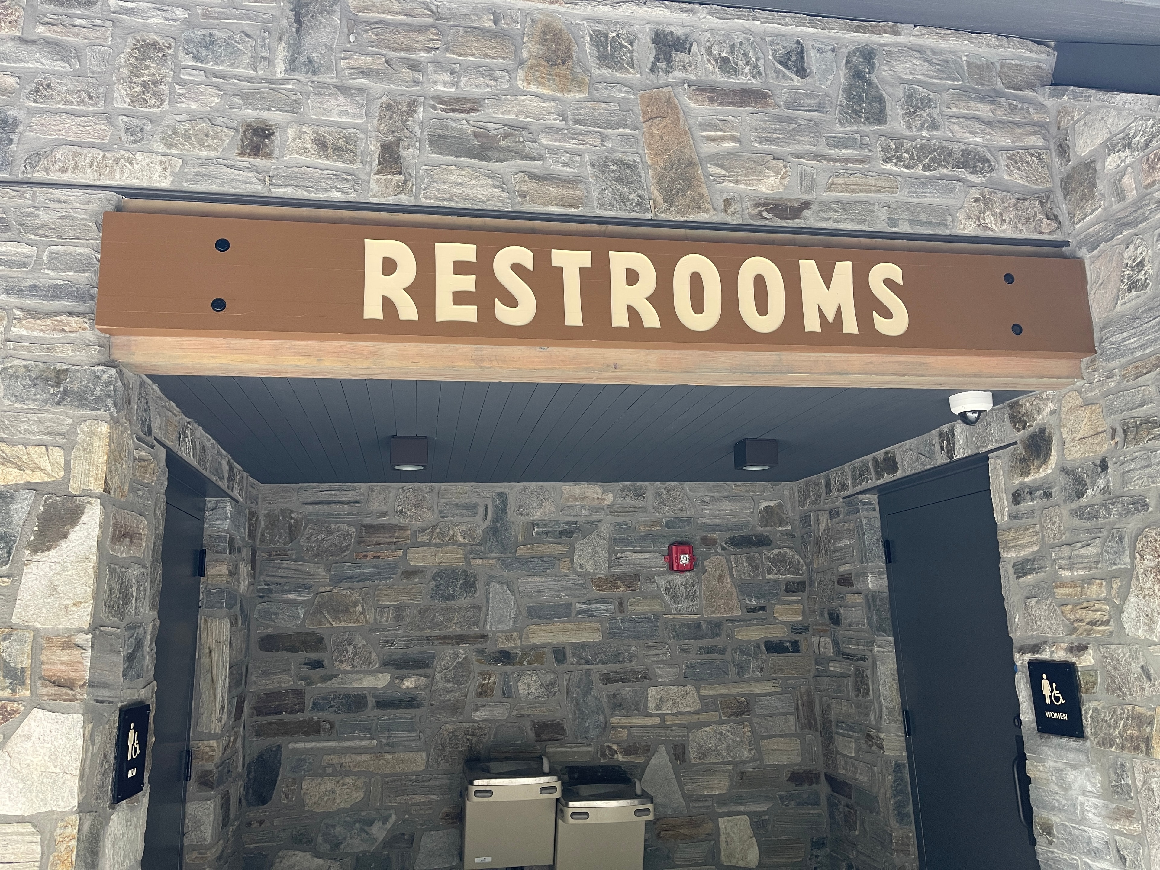 Routed wood restrooms sign with cream lettering mounted on stone exterior wall at Vogel State Park